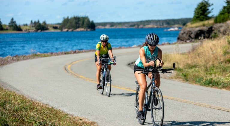two people on bikes ride by the ocean