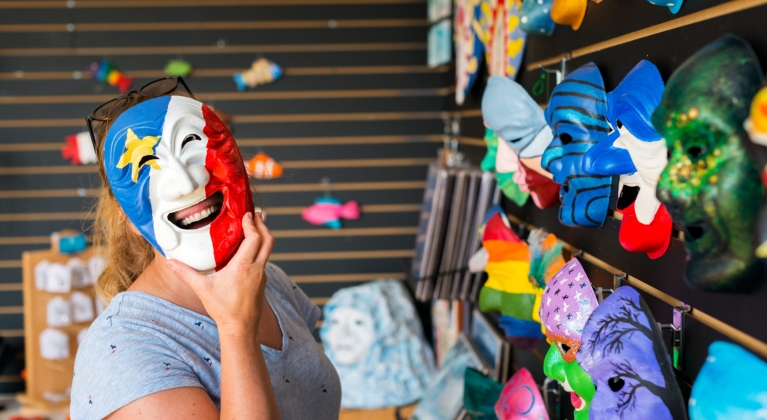 A woman holds a colourful mask over her face